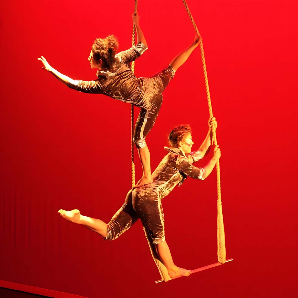 Performer standing on another performer standing on a trapeze on one foot - SHOW Circus Studio image