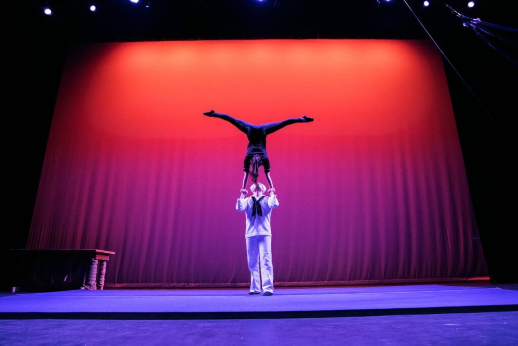 One sailor performer from SHOW Circus Studio in Easthampton, Massachusetts, supporting another doing a hand-to-hand handstand on stage